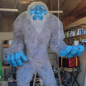 An approximately 10 foot tall 3D foam sculpture of a friendly looking blue skinned yeti with grey fur.